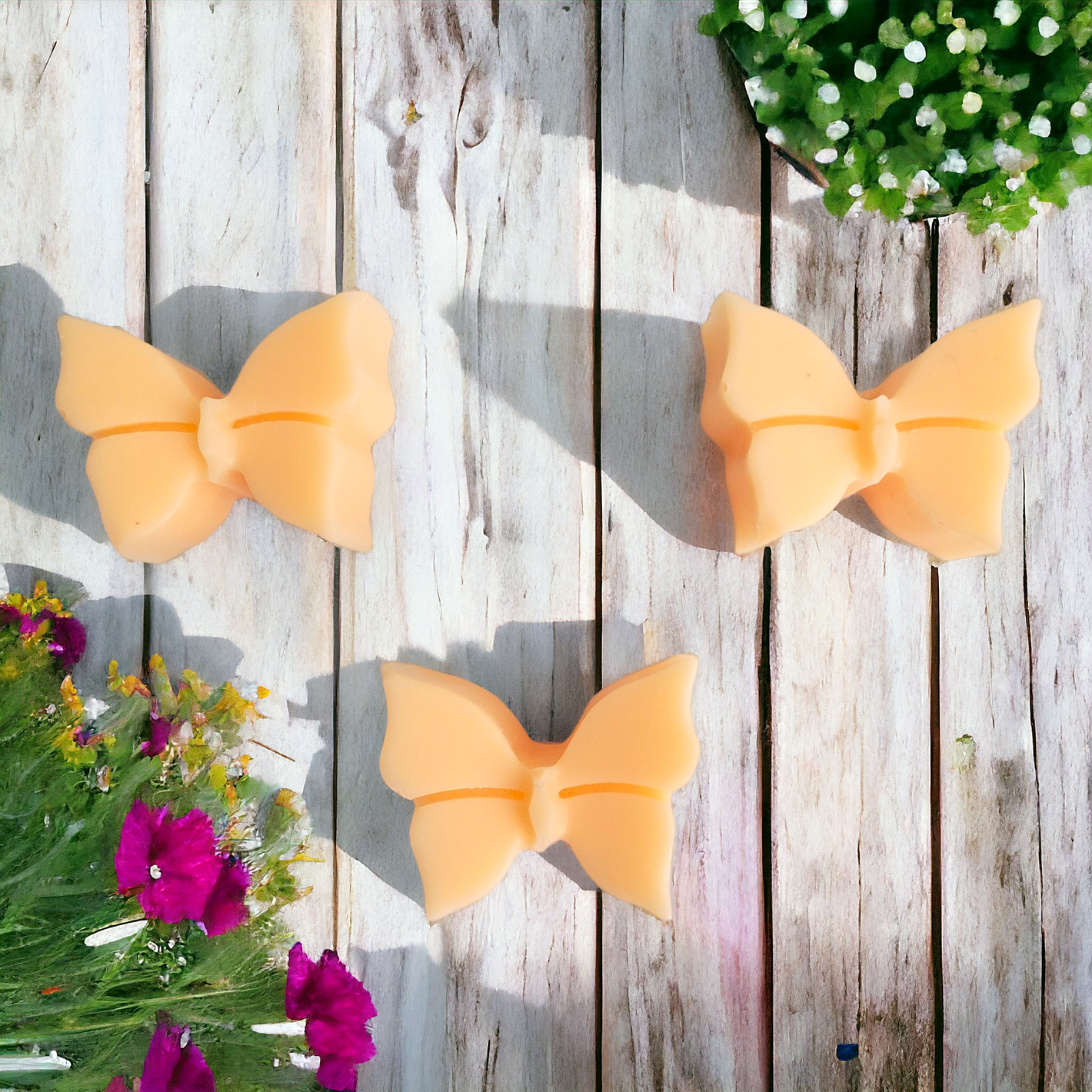 Three light orange  butterfly soy wax melts with flowers in background